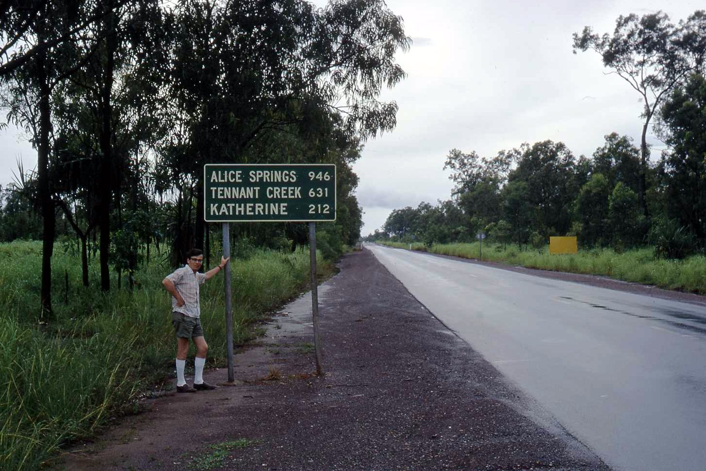Brian Collins beside a road sign to Alice Springs, Tennant Creek and Katherine, Northern Territory