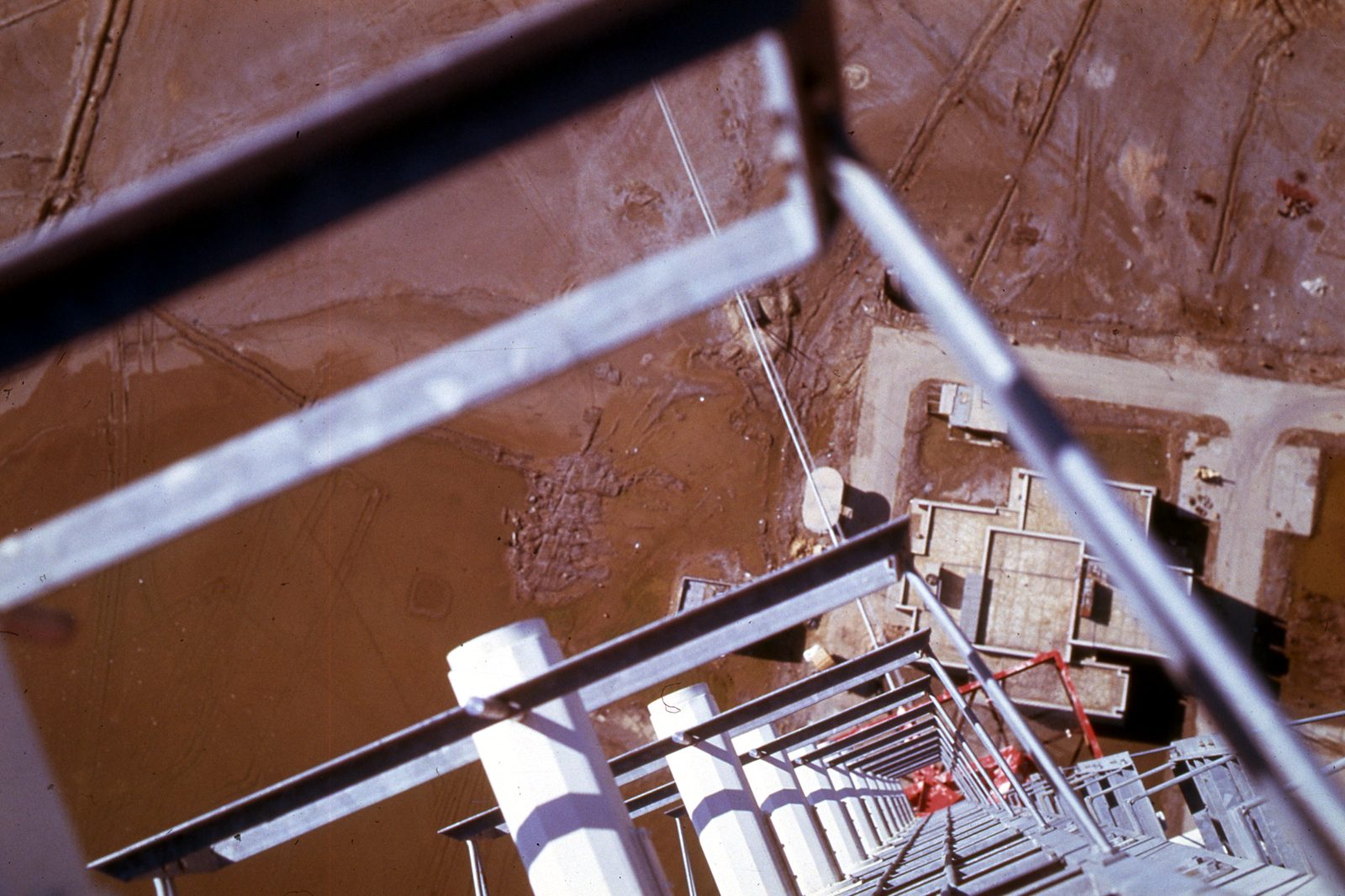 View straight down a tall lattice mast to the ground and buildings far below