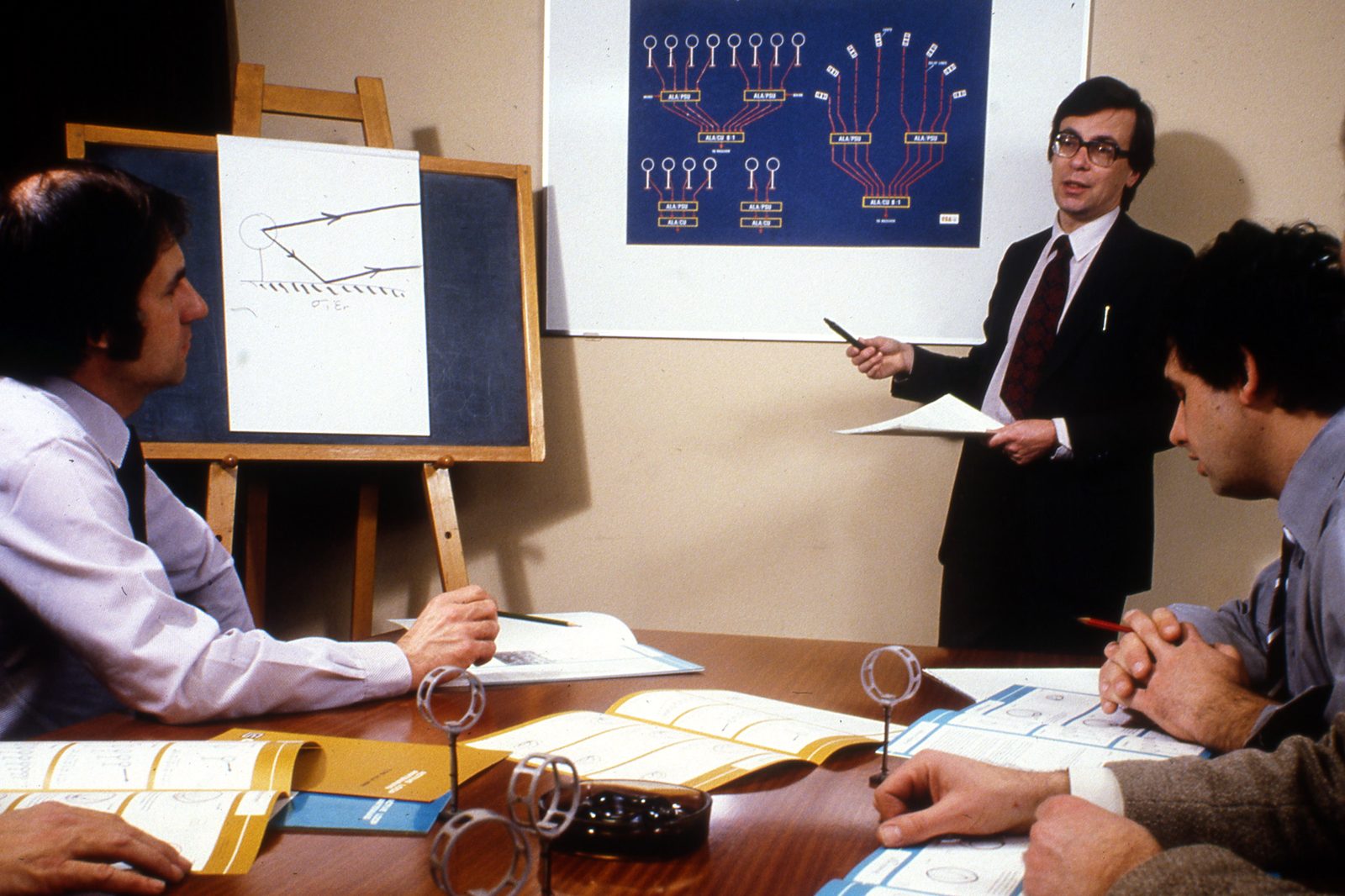 Brian Collins presenting loop array diagrams to colleagues around a table with loop antennas