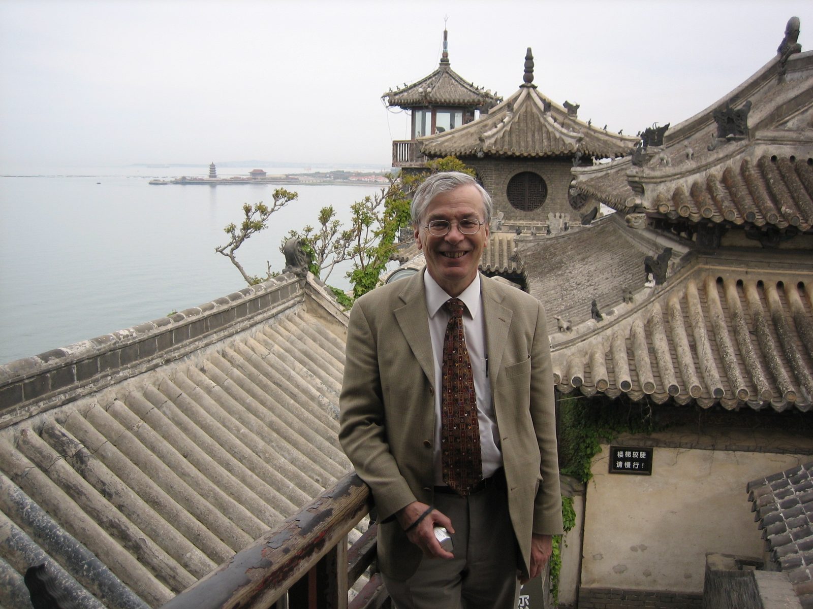 Brian Collins on a balcony above traditional Chinese tiled roofs, with the sea behind