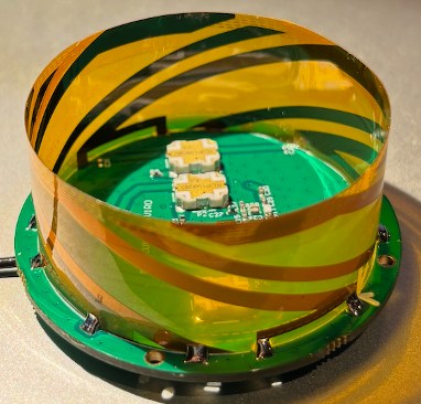 Short quadrifilar helix antenna: four helical copper strips on a transparent cylinder mounted on a circular PCB carrying the feed network