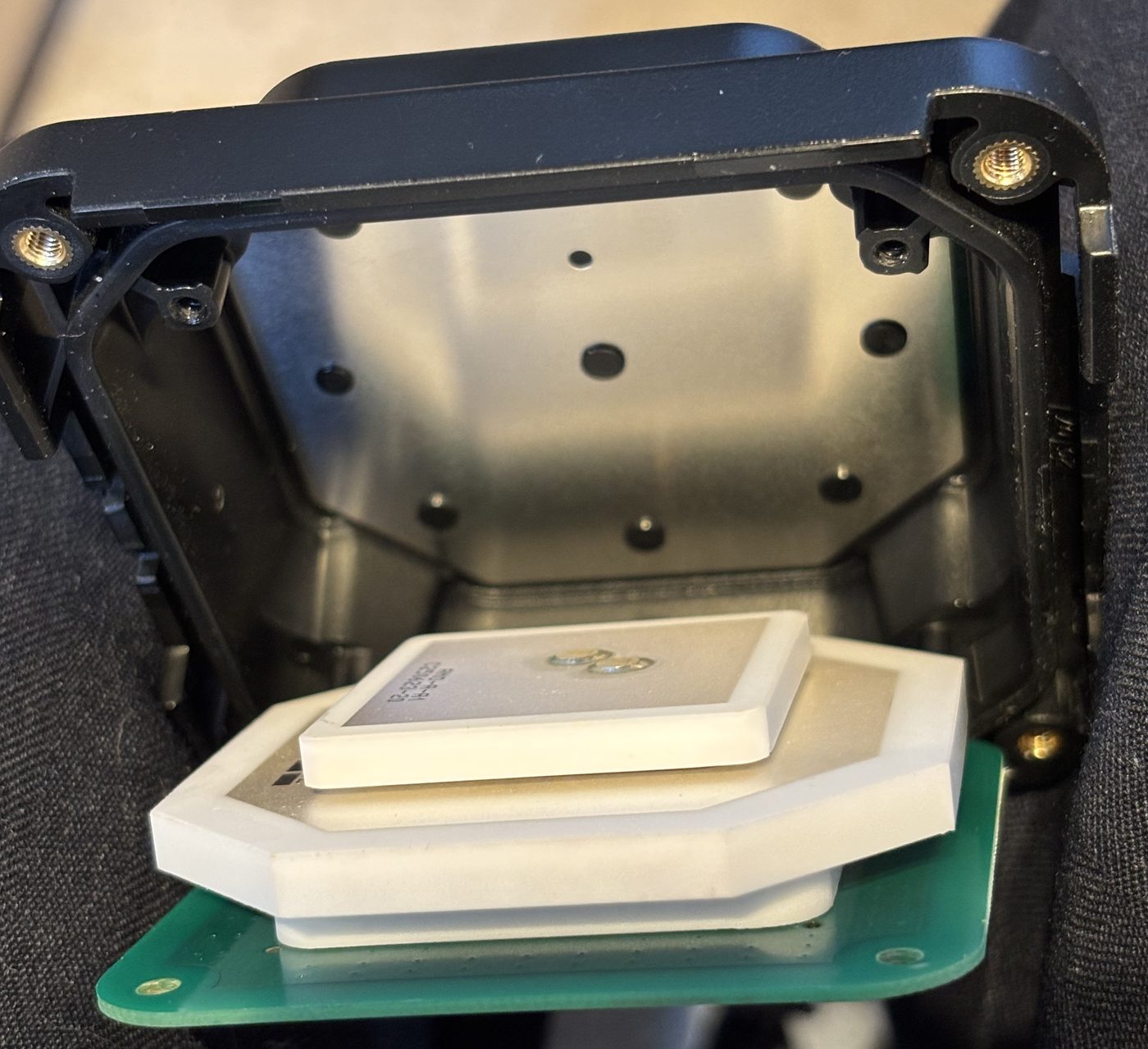 Stacked ceramic GNSS patch antenna on a green PCB, in front of its open black housing