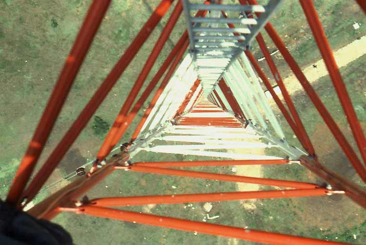 Looking down through the red steelwork of a lattice mast — a dramatic interior view of antenna-supporting structure.